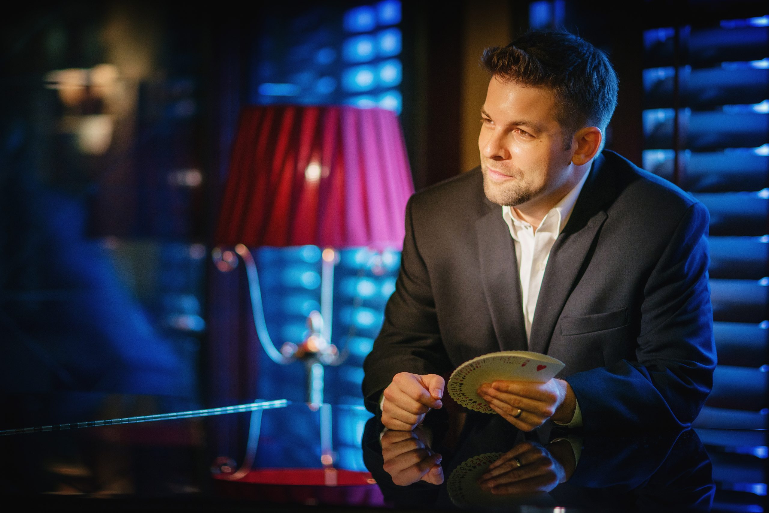 Confident businessman in suit holding playing cards beside red lamp
